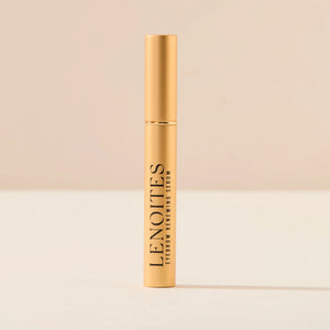Eyebrow Growth Serum by Lenoites, featuring a sleek gold tube with black text, displayed against a soft beige background.