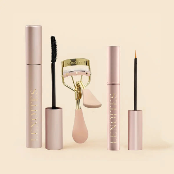 The Complete Lash Kit by Lenoites featuring a black PowerLash Growth Serum Mascara, a pink eyelash curler with gold details, and a  Eyelash Growth Serum with a fine applicator, displayed against a soft beige background.