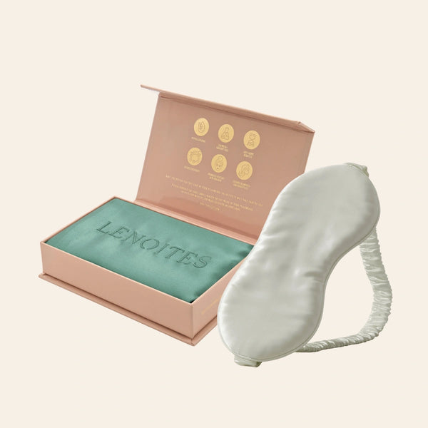Pillowcase and Sleep Mask in Mulberry Silk by Lenoites featuring a grey silk sleep mask and a green mulberry silk pillowcase presented in an open blush pink box against a soft light background.