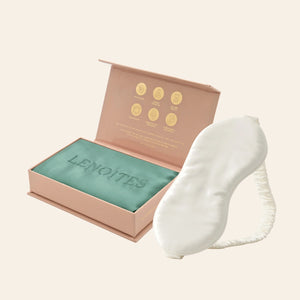 Pillowcase and Sleep Mask in Mulberry Silk by Lenoites featuring a white silk sleep mask and a green mulberry silk pillowcase presented in an open blush pink box against a soft light background.
