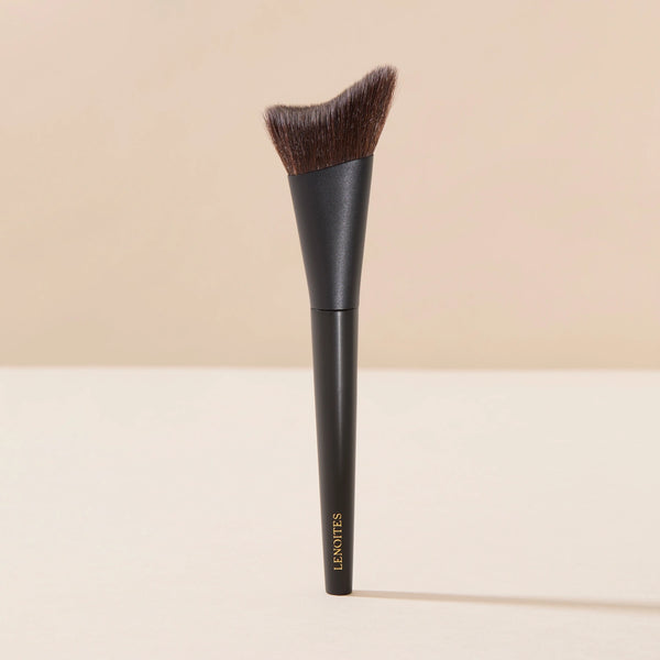 Brush Me Smoothing Foundation Brush No. 101 by Lenoites, featuring a black handle and a soft, angled brush head designed for smooth foundation application, displayed against a soft beige background.